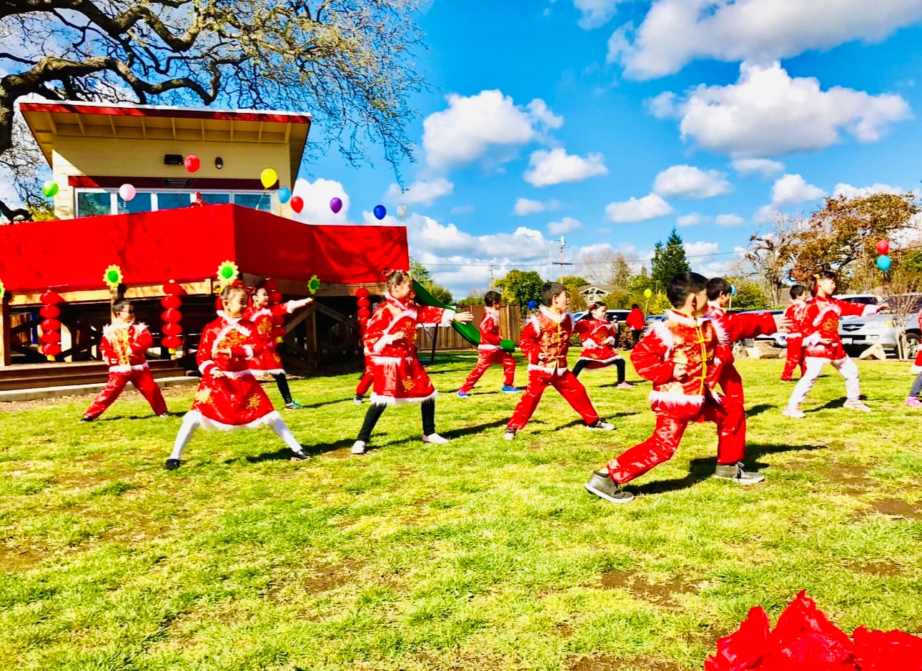 Students in red traditional costumes perform a dance on the lawn.